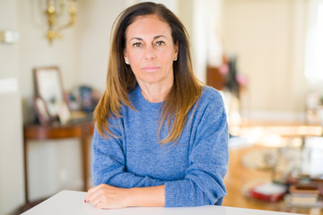 Beautiful middle age woman at home with serious expression on face. Simple and natural looking at...