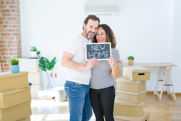 Fototapeta na wymiar Middle age senior couple moving to a new house, smiling happy in love with apartmant holding a blackboard with new home text