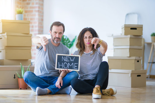 Middle age senior couple sitting on the floor holding blackboard moving to a new home with angry face, negative sign showing dislike with thumbs down, rejection concept