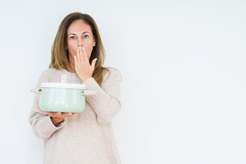 Fototapeta premium Middle age housewife woman holding iron cooking pot over isolated background cover mouth with hand shocked with shame for mistake, expression of fear, scared in silence, secret concept