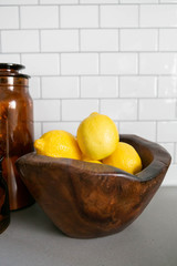 Lemons in Wooden Bowl and Amber Jars on Concrete Kitchen Countertop, White Subway Tile Backsplash