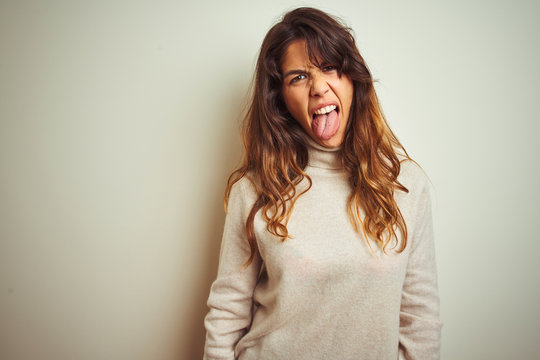 Young beautiful woman wearing winter sweater standing over white isolated background sticking tongue out happy with funny expression. Emotion concept.
