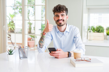 Young business man using smartphone sending a message happy with big smile doing ok sign, thumb up with fingers, excellent sign