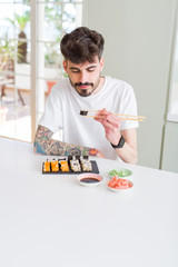 Young man eating sushi asian food using choopsticks