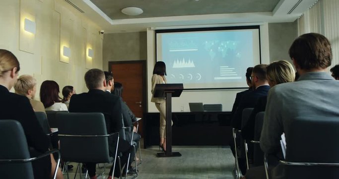 Beautiful Caucasian brunette young woman standing at the lecturn and talking to the audience about her report at the annual congress.