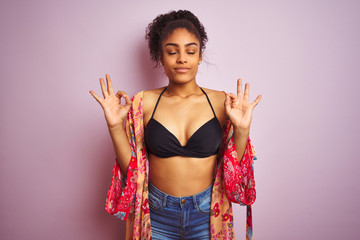 American woman on holiday wearing bikini and colorful dress over isolated pink background relax and...