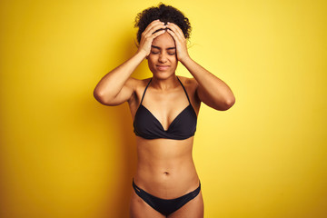 African american woman on vacation wearing bikini standing over isolated yellow background suffering from headache desperate and stressed because pain and migraine. Hands on head.
