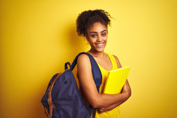 Fototapeta American student woman wearing backpack holding notebook over isolated yellow background with a happy face standing and smiling with a confident smile showing teeth obraz
