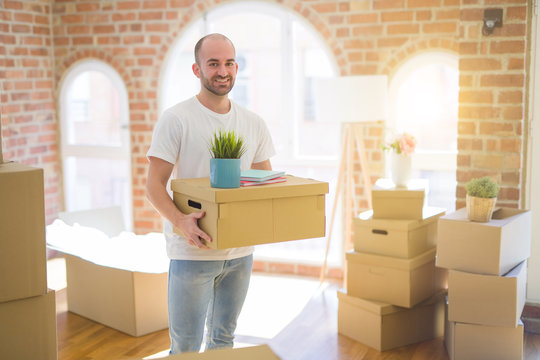 Young handsome man moving to a new house, holding cardboxes smiling very happy for new apartment