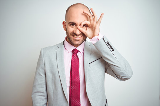 Young business man wearing suit and purple tie over isolated background doing ok gesture with hand smiling, eye looking through fingers with happy face.