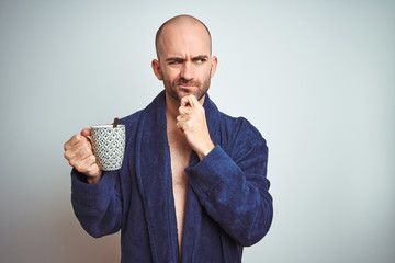 Young man wearing a bathrobe drinking a cup of coffee in the morning over isolated background...