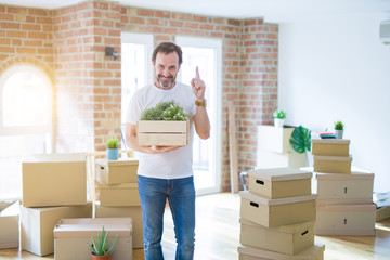 Middle age senior man moving to a new house packing cardboard boxes surprised with an idea or question pointing finger with happy face, number one