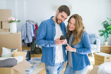 Young couple moving to a new house using smartphone around cardboard boxes