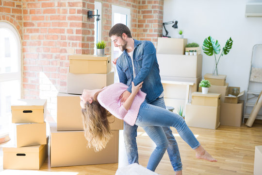 Young couple dancing celebrating moving to new apartment around cardboard boxes