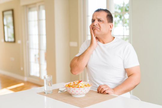 Middle age man eating rice at home thinking looking tired and bored with depression problems with crossed arms.