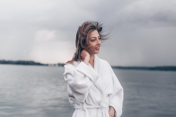 a girl in a white coat on the waterfront by the water.cloudy weather