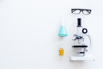 Laboratory desk with glasses, pills in test tube and microscope on white background top view space for text