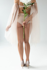 cropped view of delicate young woman in beige lingerie and mesh sleeves holding bouquet of lilies isolated on white
