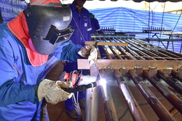 The welder is welding the plate to the pipe with Tungsten Inert Gas Welding process (TIG). The welder wears protective equipment with a mask and heat resistant gloves