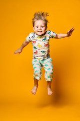 Little cute blond boy preschooler in pajamas with dinosaurs having fun has joy in the studio over yellow background.