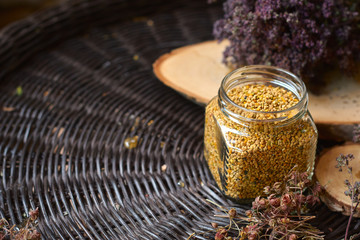 A table with a wicker table top, honey in honeycombs on a wooden board, honey in an open glass jar, with medicinal herbs oregano, chamomile and strawberry flowers. flower pollen collected by bees