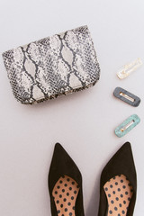 Fashionable hairpins, a snakeskin bag with an animal print and black women's shoes on a beige pastel background. The concept of style and women's accessories