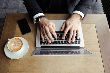 hands men lie on the laptop, near a phone and cappuccino