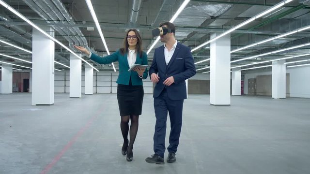 Commercial real estate concept. Businessman in VR-glasses is walking with a female manager along the hall