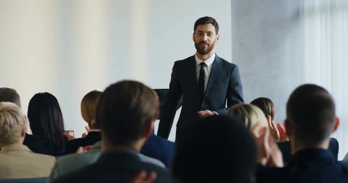 Caucasian handsome youg business coach having his speech at the conference and pointing at someone from the audience, then coming closer to that woman.