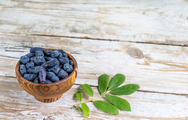 Ripe honeysuckle berries in a wooden bowl on wooden boards. Summer still life of honeysuckle berries. copy space.