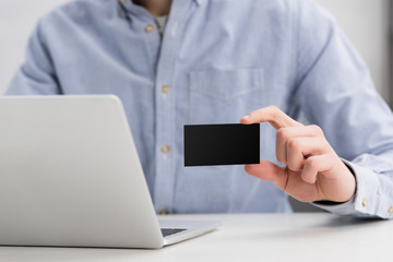 cropped view of businessman holding empty black business card while sitting at workplace