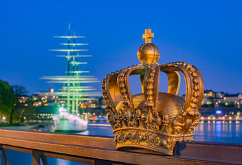 Fototapeta na wymiar Golden crown on Skeppsholmen bridge with illuminated Stockholm old city