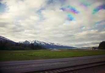 Small airport runway in Alaska's interior with cloudy sky and snowy mountains