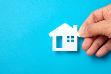 Hand hold a paper house on blue background for real estate property industry