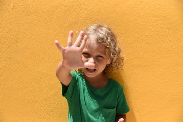Portrait of blond curly cute boy of 4-5 years on an orange wall background, showing five fingers