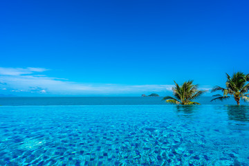 Fototapeta na wymiar Beautiful luxury outdoor swimming pool in hotel resort with sea ocean around coconut palm tree and white cloud on blue sky