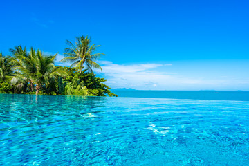 Fototapeta na wymiar Beautiful luxury outdoor swimming pool in hotel resort with sea ocean around coconut palm tree and white cloud on blue sky