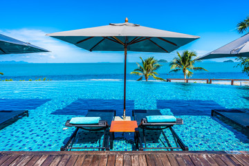 Fototapeta premium Beautiful luxury outdoor swimming pool in hotel resort with sea ocean around coconut palm tree and white cloud on blue sky