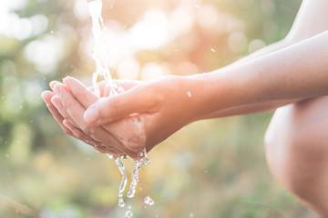 Water from tap to woman hand in nature green park sunset time and bokeh sun light abstract...