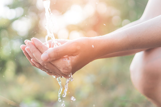 Water From Tap To Woman Hand In Nature Green Park Sunset Time And Bokeh Sun Light Abstract Background.