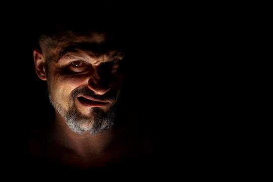  Face With A Bearded Man Grimace Against A Dark Background With Sharp Shadows. Comedic, Fabulous Villain Or Negative Character Conception With Copy Space.