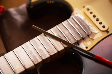 Refretting an electric guitar. Electric guitar in  a guitar repair shop with file on fret. Double...