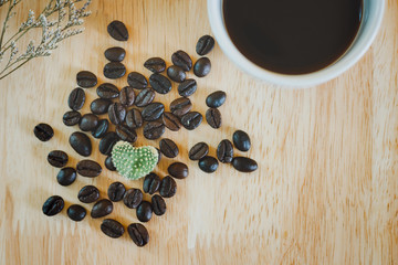 Top view. closeup of cactus heart shape on coffee bean with black coffe and dry leaf on wooden table. vintage tone