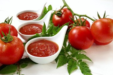 Tomato Sauce.Homemade tomato sauce in a white sauce-pan set and fresh ripe tomatoes with leaves on a white wooden background.