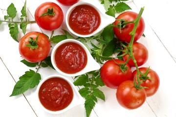 Tomato Sauce.Homemade tomato sauce in a white sauce-pan set and fresh ripe tomatoes with leaves on a white wooden background.top view