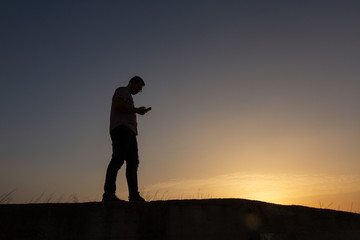 silhouette of man with cell phone at sunset