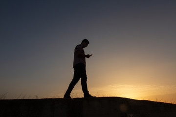 silhouette of man with cell phone at sunset