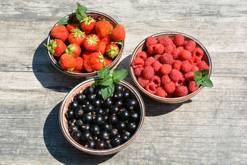 Three clay cups with berries strawberries,raspberries,currants and sprigs of mint