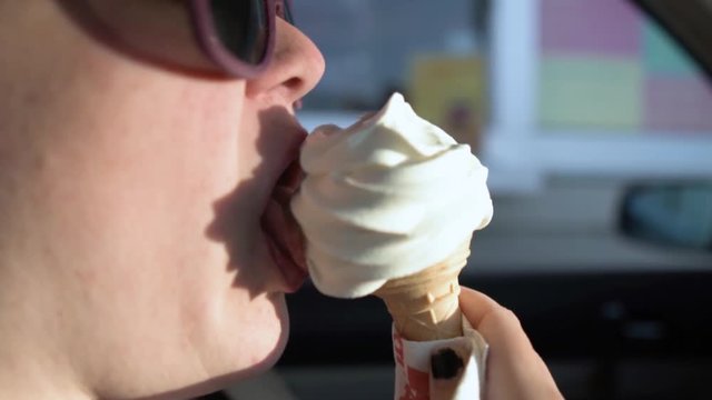 Woman eating an ice-cream while sitting in a car next to a drive-trough.
