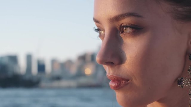 Beautiful model woman looking to the sun on sunset near the water. Woman face close up shot on sunset near the ocean. Beautiful eyes